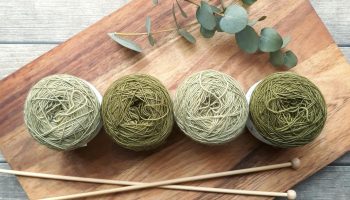 A flat lay of green yarn balls and knitting needles on wood, evoking creativity and craftsmanship.