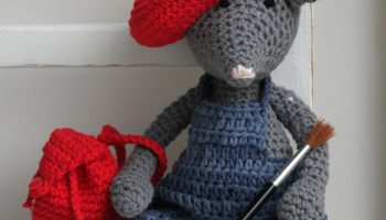 A charming crochet mouse toy dressed as an artist holding a paintbrush, complete with a red beret.
